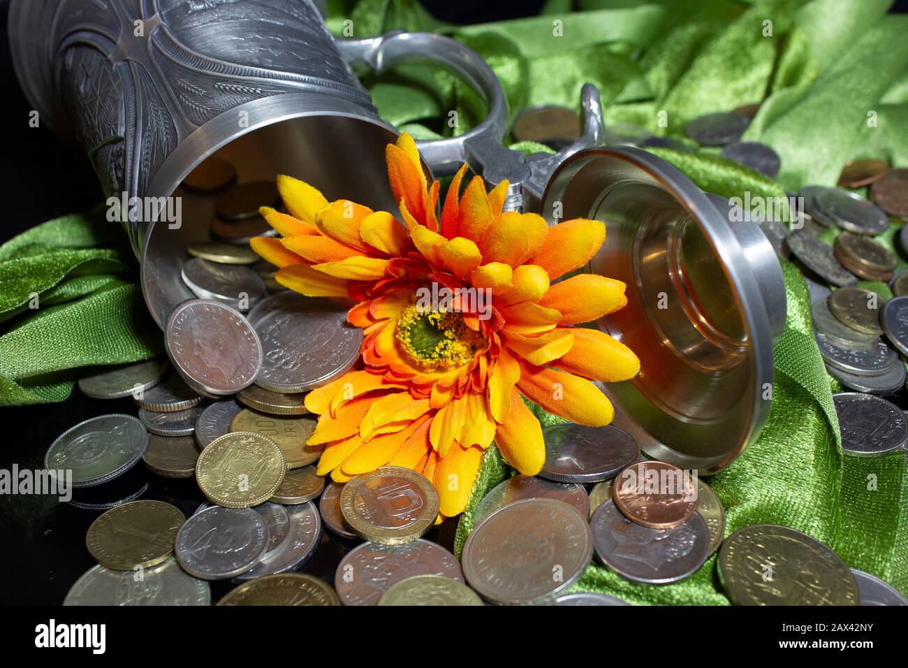 Blumenblätter aus Stoff, umrahmt von einem Zinnbecher mit alten Münzen Stockfoto