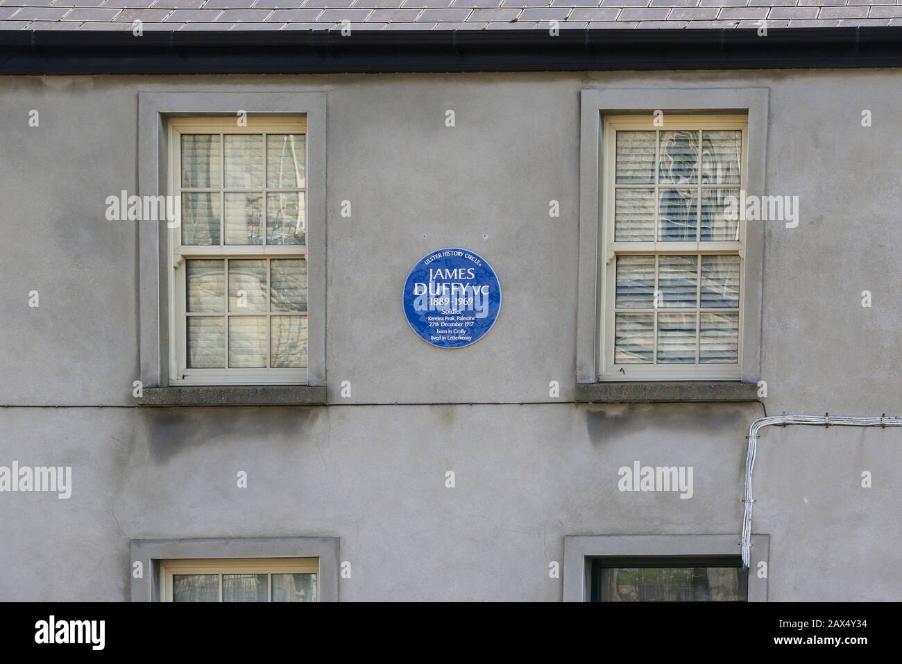 Eine runde blaue Geschichtsplakette zwischen zwei Holzfenstern an der Wand eines Gebäudes in Letterkenny, County Donegal, erinnert an James Duffy VC. Stockfoto