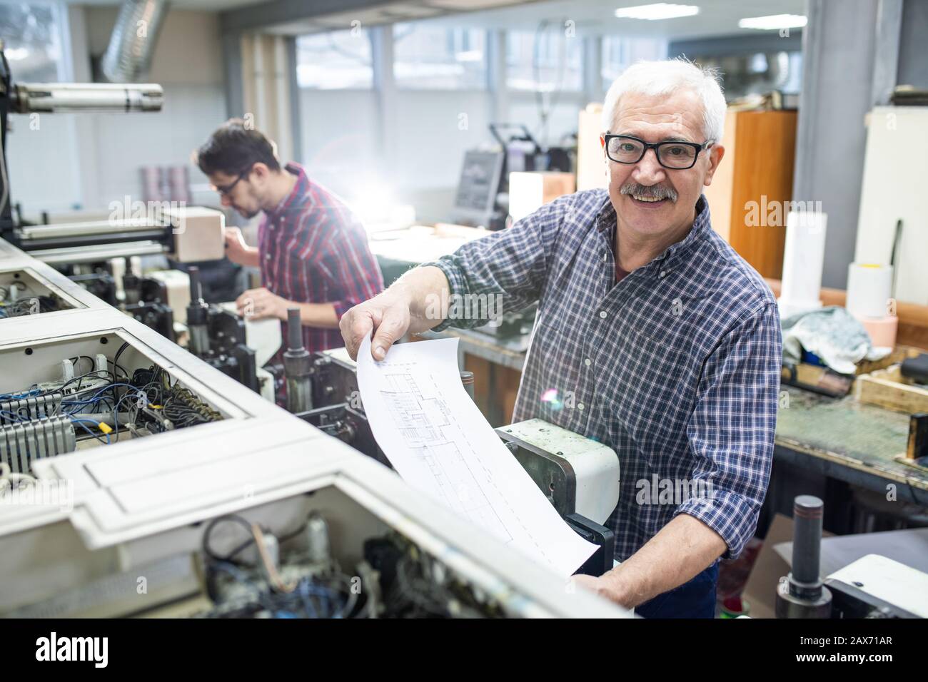 Porträt eines fröhlichen Seniors in einer Brille Druckpapier aus der Druckmaschine in der Fabrik Stockfoto