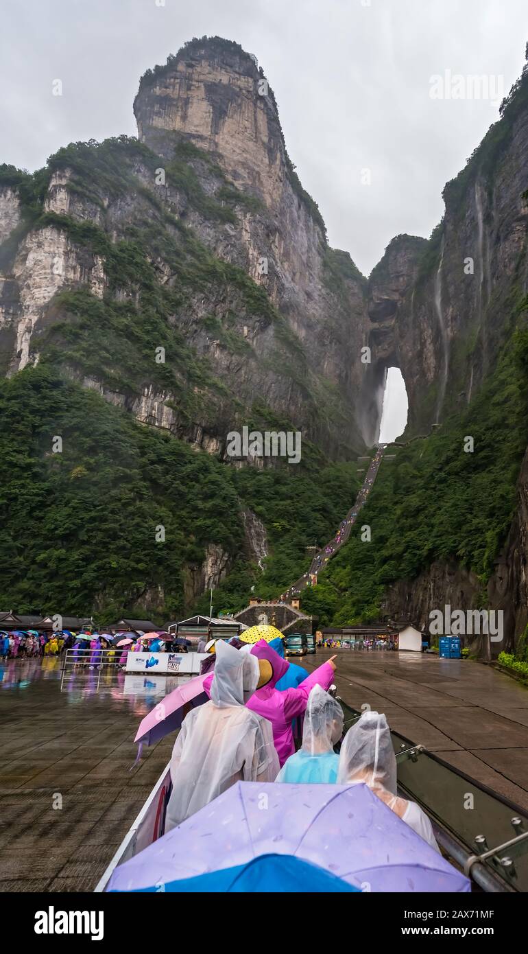 Zhangjiajie, China - August 2019: Massive Touristenmassen, die im sintflutartigen Monsunregen auf Kleinbusse des öffentlichen Verkehrs am Fuß des Tianmen M warten Stockfoto