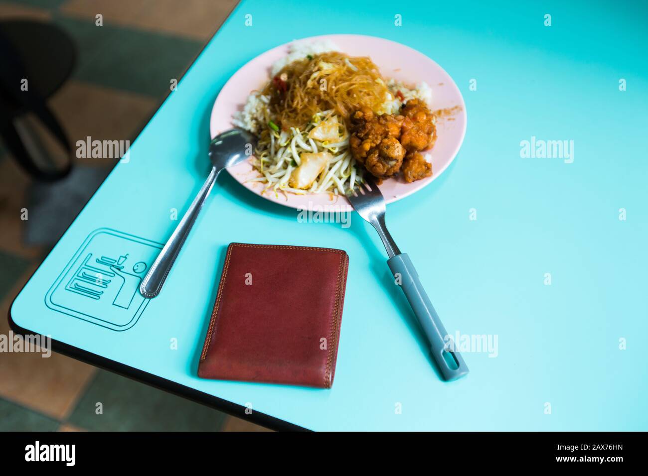 Eine unbeaufsichtigte braune Farbtasche neben einem Teller gemischter chinesischer Reismahlzeit am Rand des Tisches. Stockfoto