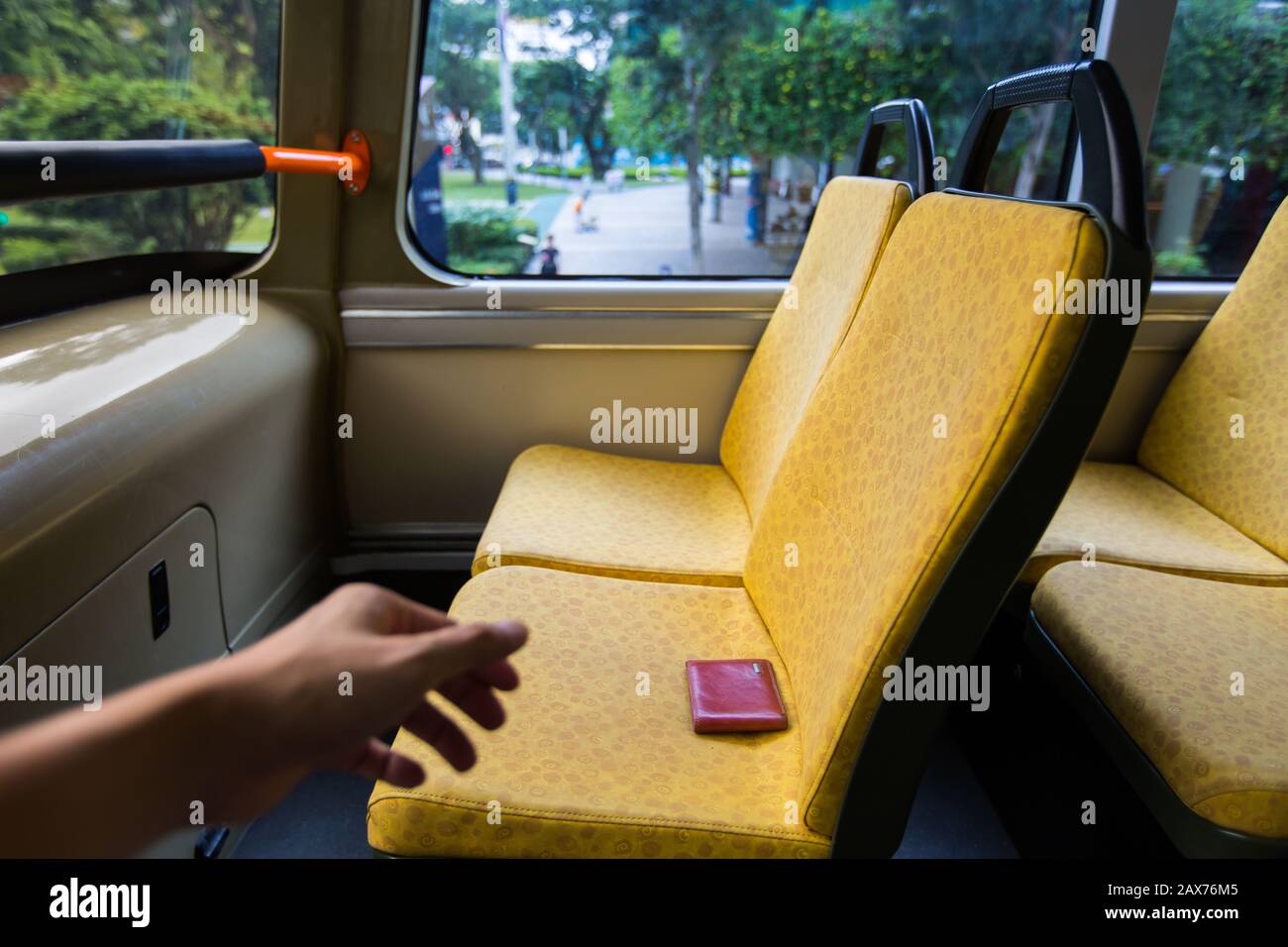 Eine linke Hand streckt sich aus, um eine verlorene Geldbörse auf dem Sitz eines öffentlichen Busses zu holen. Stockfoto