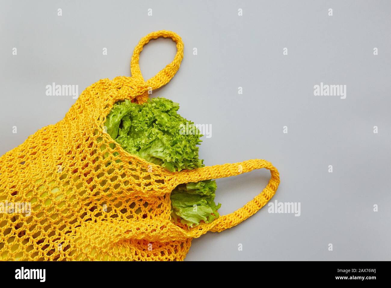 Stricktasche mit Salat auf grauem Hintergrund und Platz für Kopien. Einkaufen von Speisen mit umweltfreundlicher Tasche. Pflege der Umwelt, Ablehnung von Kunststoff, ze Stockfoto