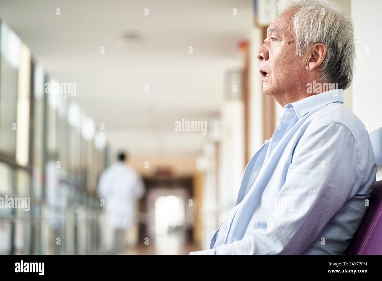 Asiatischer alter Mann, der auf dem Flur des Krankenhauses sitzt, sieht traurig und depressiv aus Stockfoto