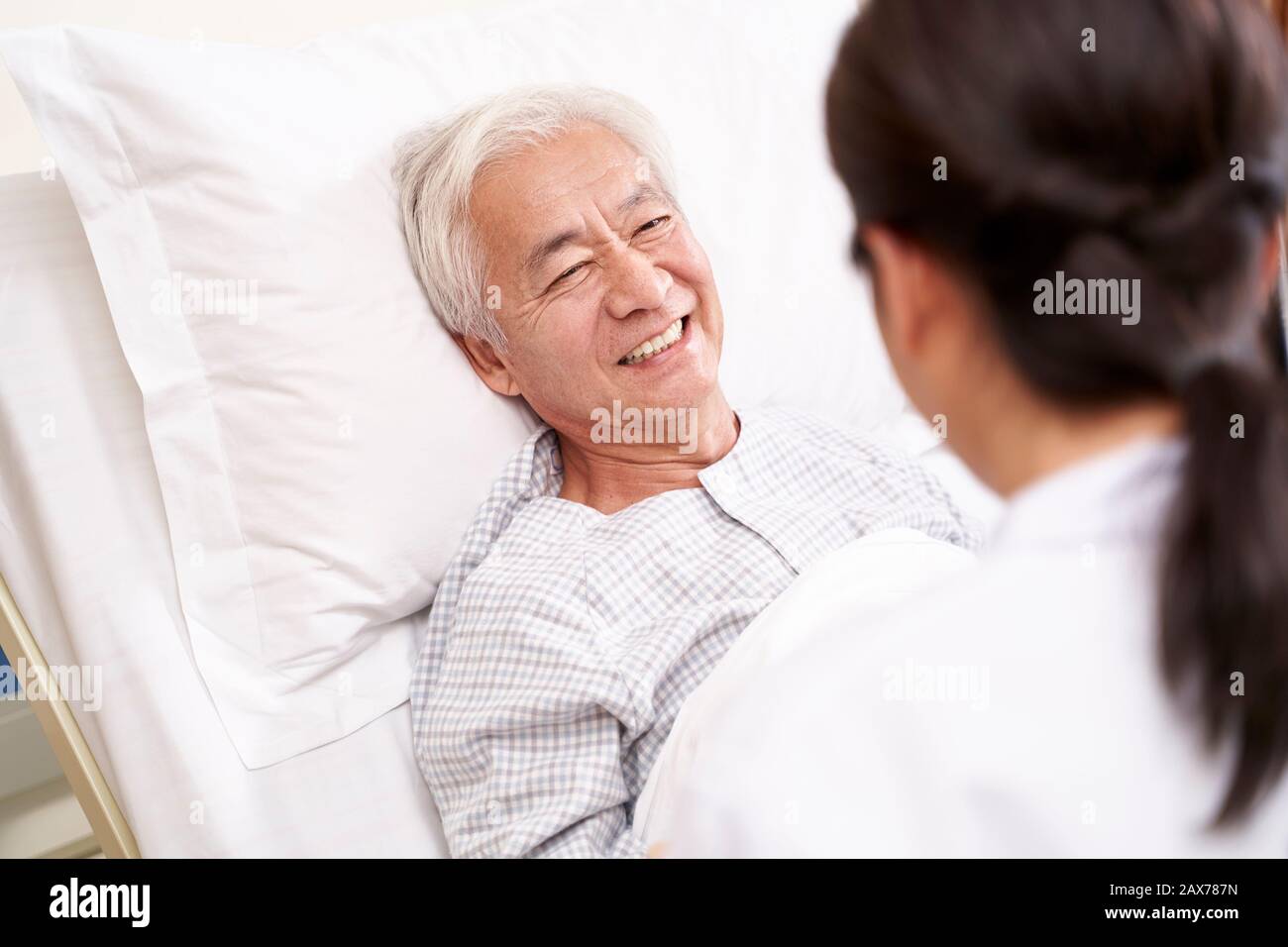 Asiatischer alter Mann, der im Bett liegt und mit junger Ärztin in der Krankenstation spricht Stockfoto Asiatischer alter Mann, der im Bett liegt und mit junger Ärztin in der Krankenstation spricht Stockfoto