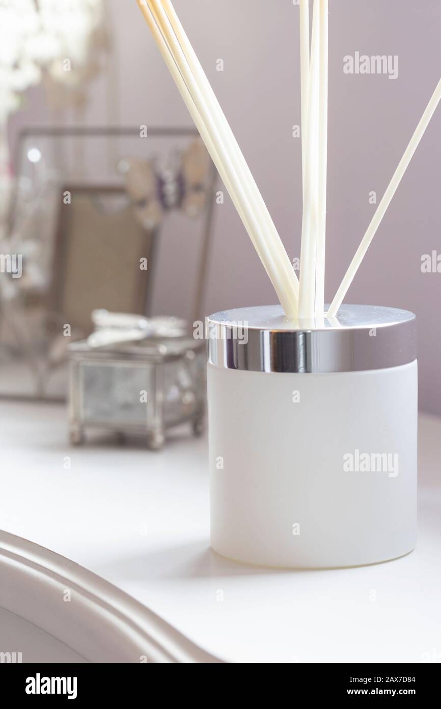 Reed-Diffusor mit Stöcken in einem Milchglasbecher auf einer weißen Seitenwand mit Verzierungen Stockfoto