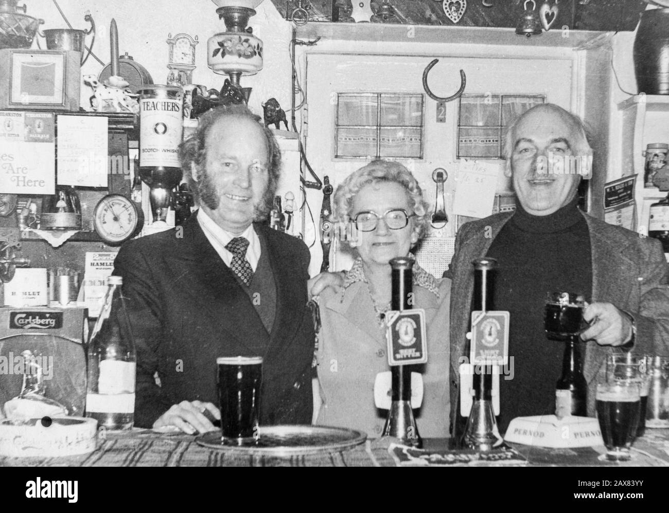 Die Emmerdale Schauspieler Ronald Magill (links) und Arthur Pentelow (rechts) hinter der Bar im White Bear Pub in Masham, Yorkshire, mit Landfrau Mary Gray. Stockfoto