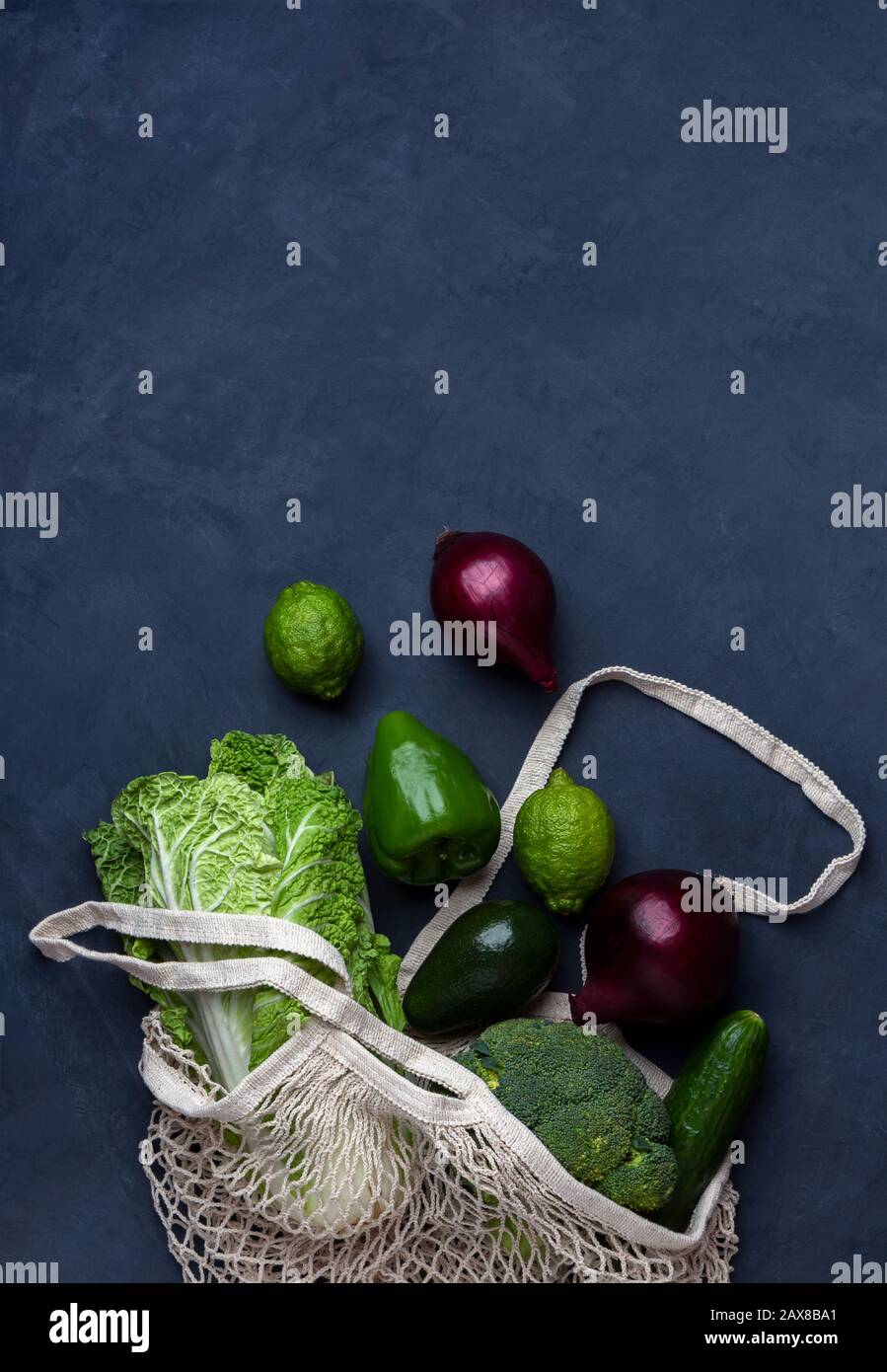 Grünes Gemüse und Obst in einer wiederverwendbaren Netztasche auf blauem Hintergrund. Null-Abfall-Konzept mit Kopierraum. Stockfoto