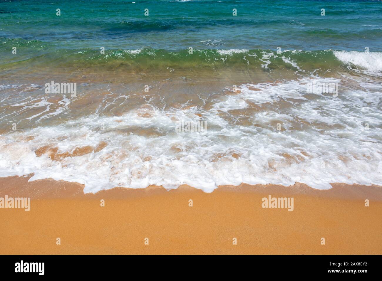 Wellen am Strand mit orange Sand und blauem Wasser Stockfoto