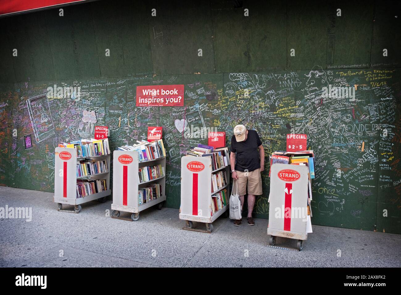Ein Kunde in der Buchhandlung Strand durchsucht Verkaufsbücher vor einer interaktiven Wand, die fragt, "Welches Buch inspiriert Sie? In Manhattan, NYC. Stockfoto