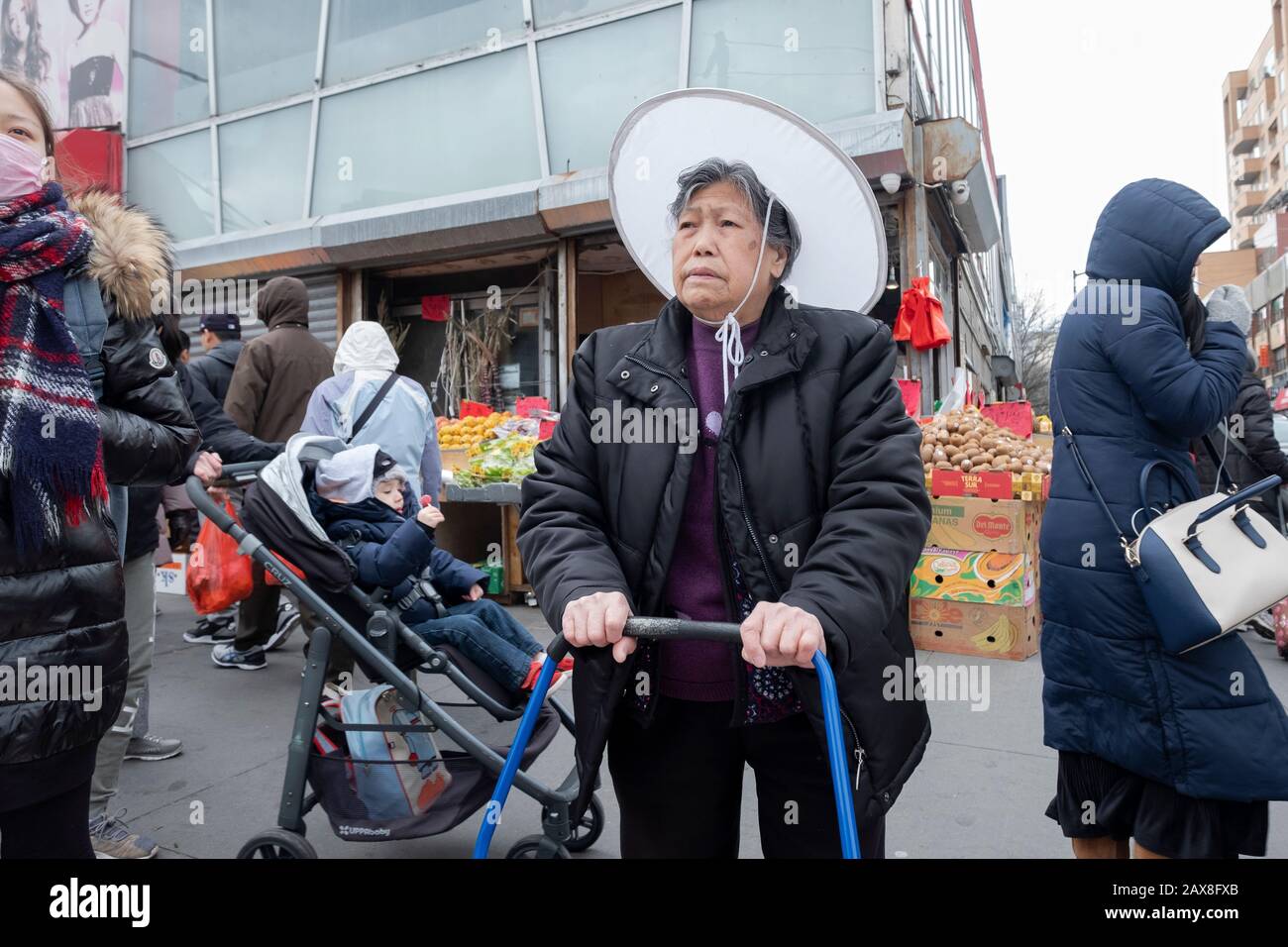 Auf einer Einkaufsbummel durch das Essen wartet eine ältere Amerikanerin in einem großen runden Hut, die Main St. in Chinatown, Flushing, Queens, New York City überquert. Stockfoto