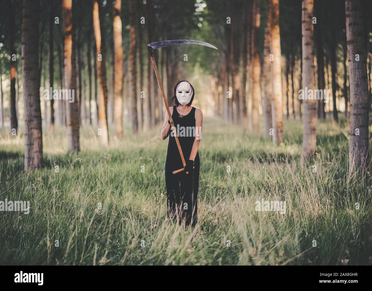 Junge Frau mit Schythe und Maske im Wald Stockfoto