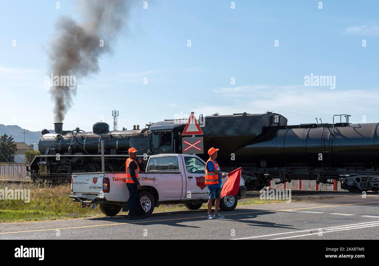 Wolseley, Region Swartland, Südafrika. 2019. Mann mit roter Flagge hält Verkehr. Dampfzug mit Dieselantrieb über die Autobahn in Wolseley. Südafrika Stockfoto