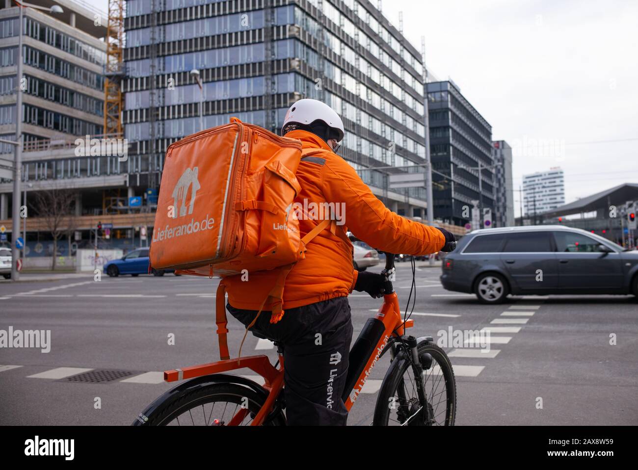 Ein Lieferando-Kurier, der in einer leuchtend fluoreszierenden orangefarbenen Uniform gekleidet ist, fährt mit dem Fahrrad, um Lebensmittel an einen Kunden zu transportieren Stockfoto