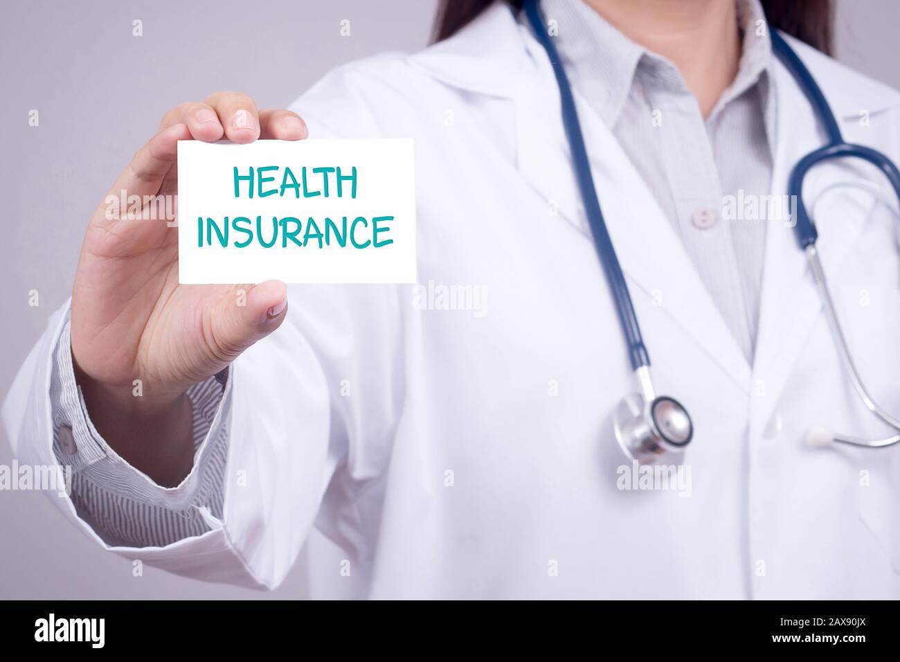 Konzept der Krankenversicherung: Arzt in der medizinischen Kleidung mit Stethoskop, das eine Karte für die Krankenversicherung in der Hand zeigt, anonyme Gesichter Stockfoto