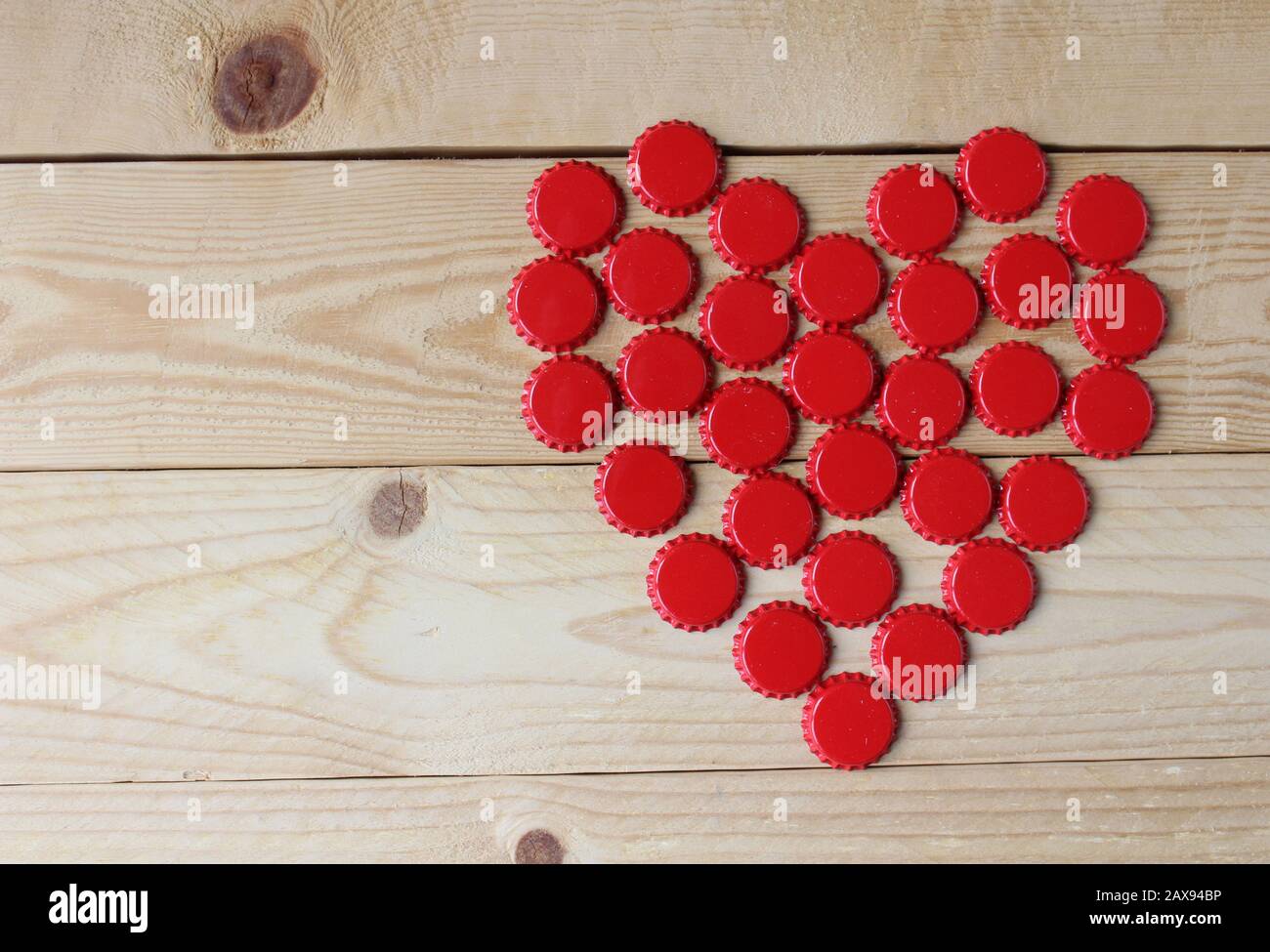 Ein rotes Liebesherz aus Bierflaschenoberteilen, oben auf einem rustikalen Holztisch betrachtet. Bier trinkt Valentinstag Konzept Stockfoto