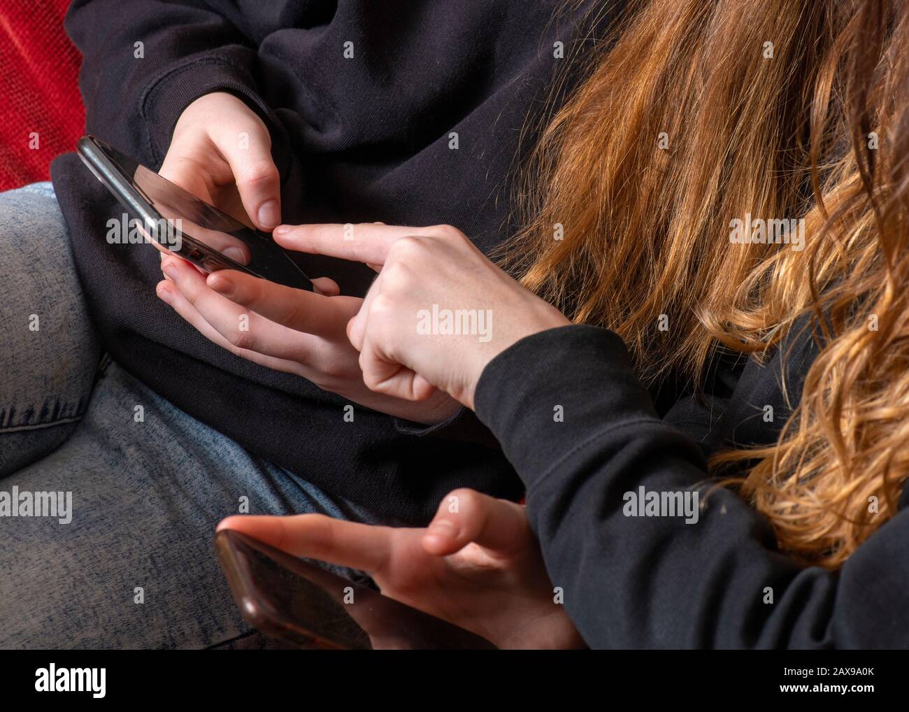 Jugendliche auf ihrem Handy, die Informationen miteinander teilen, könnten Mobbing oder soziale Medien in Schulschwitzshirts kopierten Platz oben sein Stockfoto