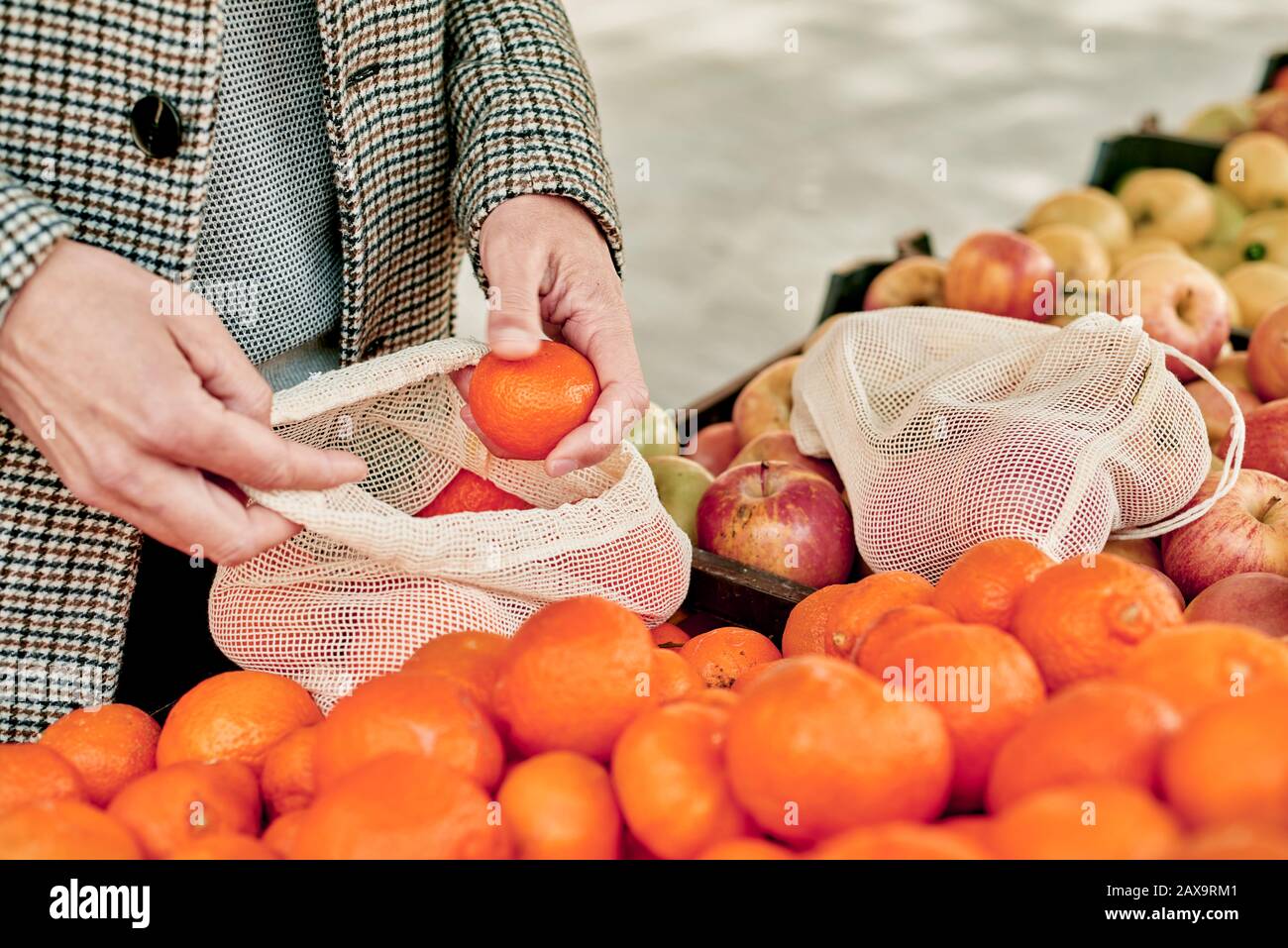 Nahaufnahme eines Mannes, der in einem Greengrocker einkauft und einige Mandarinorangen in einen wiederverwendbaren Textil-Netzbeutel einbringt, um die Kunststoffverschmutzung zu verringern Stockfoto