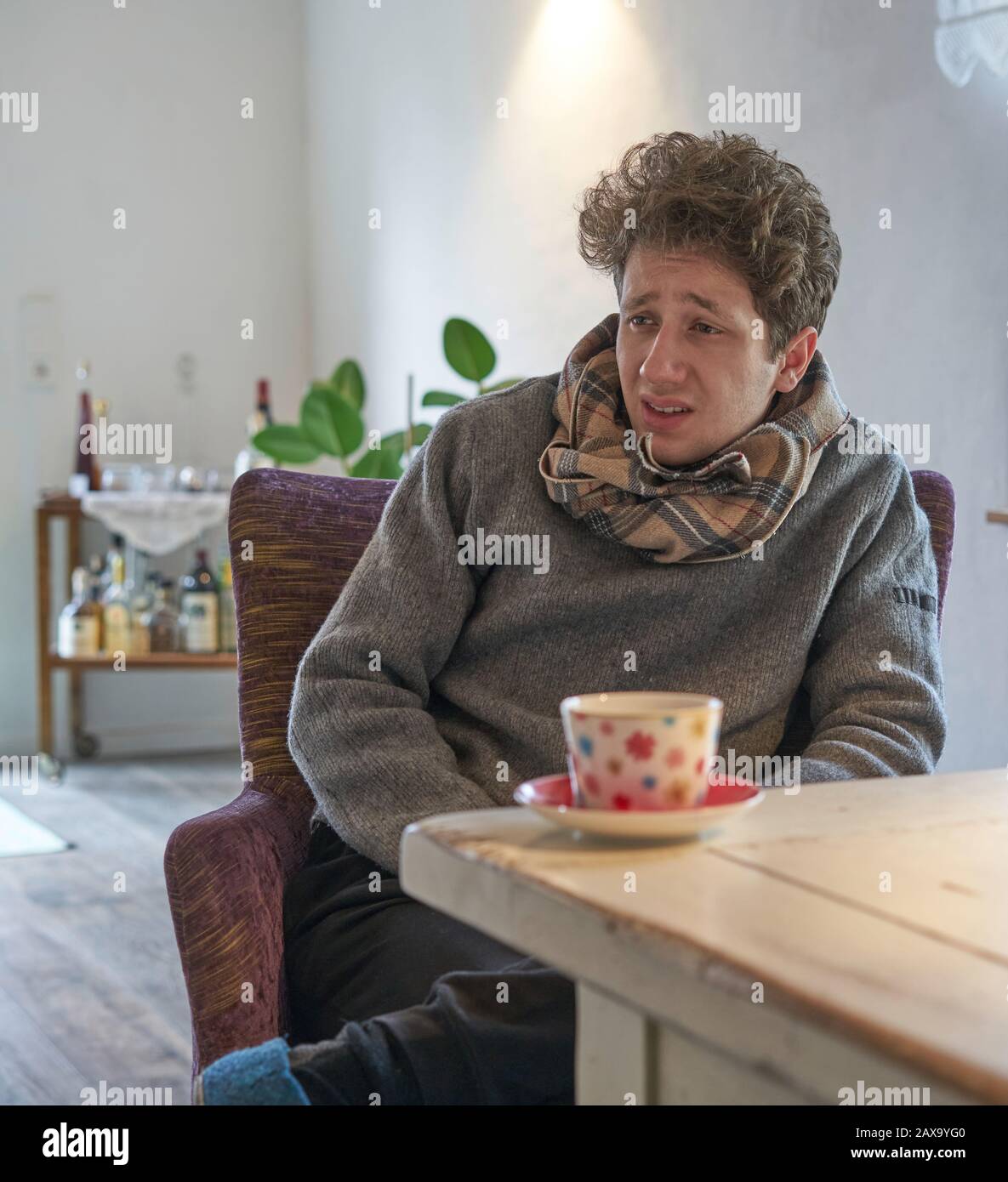 Das Porträt des jungen Studenten, der krank kalt ist, sitzt am Tisch in seiner Wohnung vor einer Tasse Tee Stockfoto