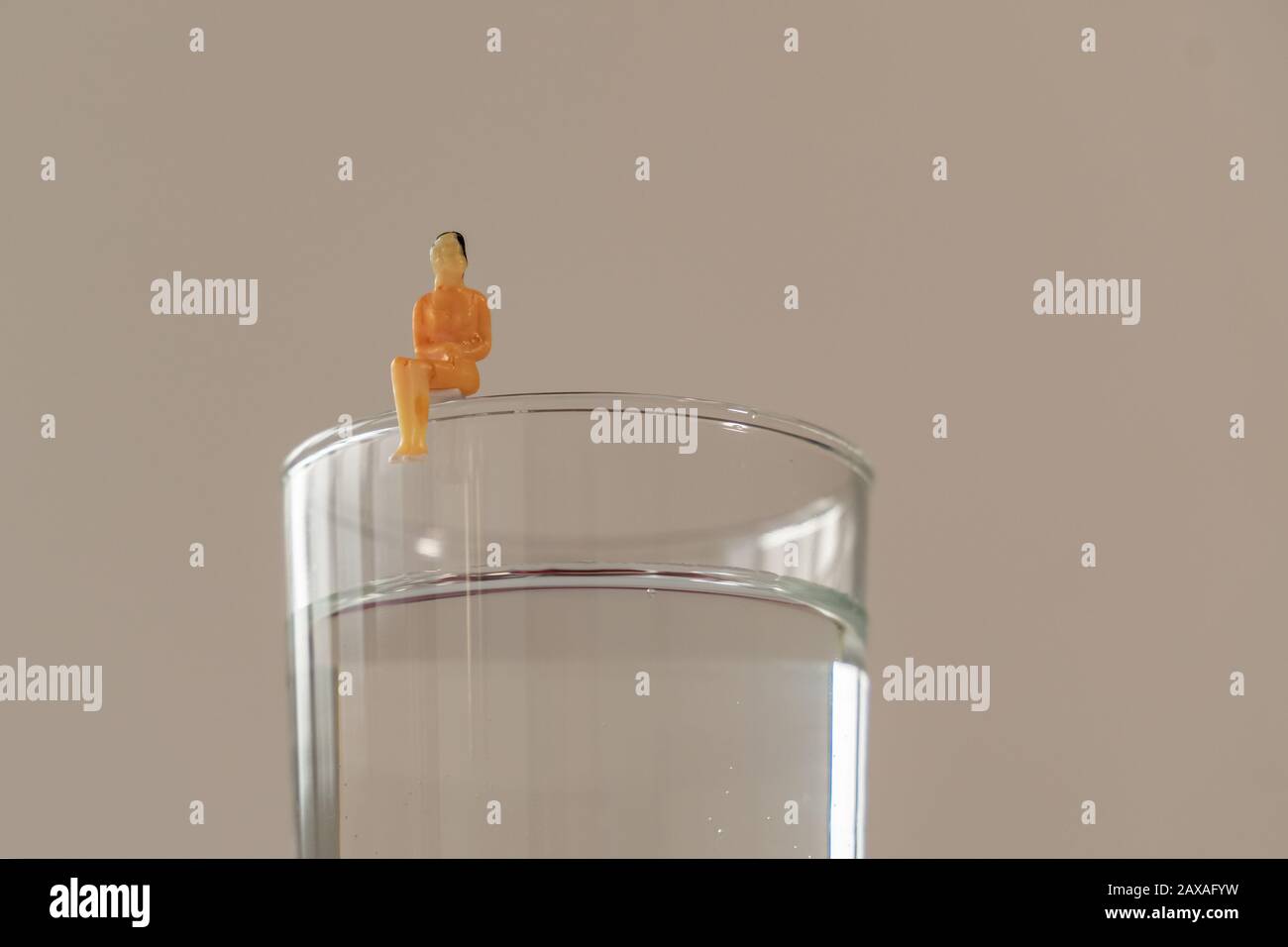 Miniaturfigur der Frau, die auf dem Glas Wasser sitzt. Geringe Tiefe des Feldhintergrunds. Gesundheitswesen, gesunder Lebensstil und schlankes Konzept. Stockfoto