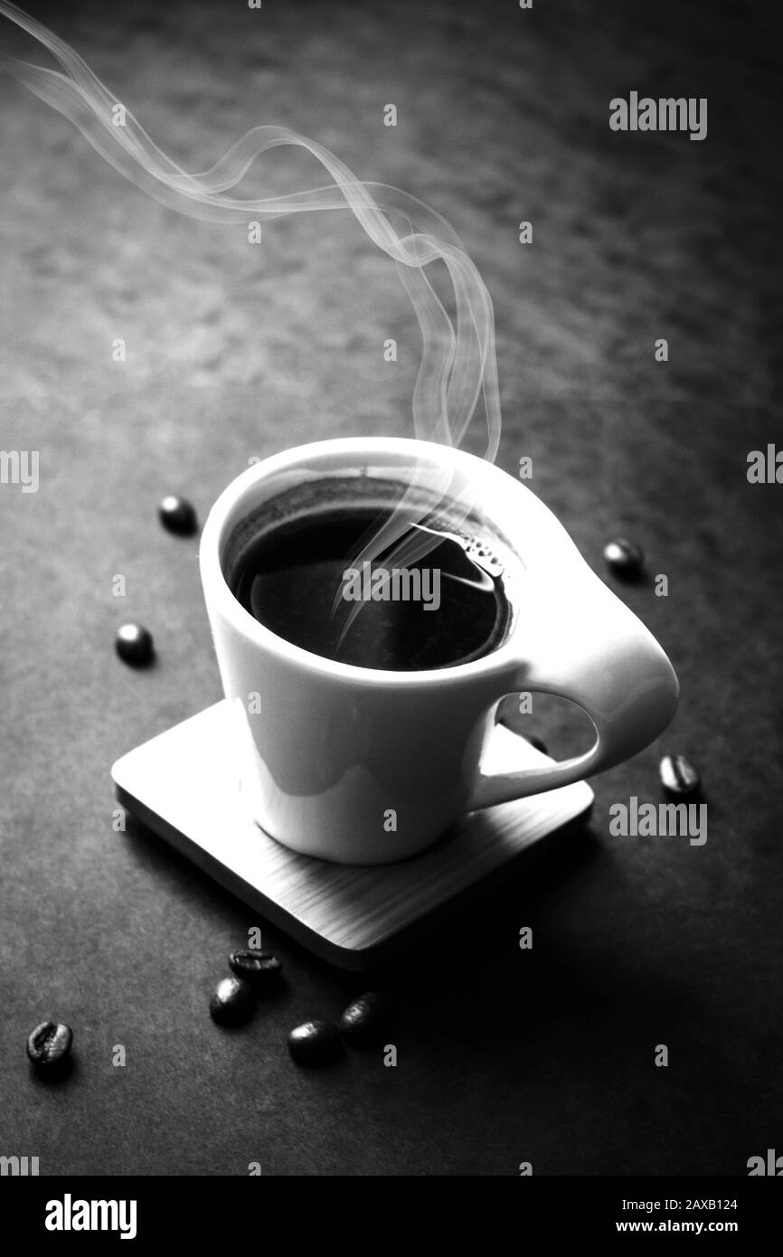 Kleine Tasse Kaffee oder Espresso am Morgen auf schwarzem Hintergrund. Um ihn herum breiteten sich nur wenige Kaffeebohnen aus. Dampfaroma steigt aus dem Becher. Schwarz und Whi Stockfoto