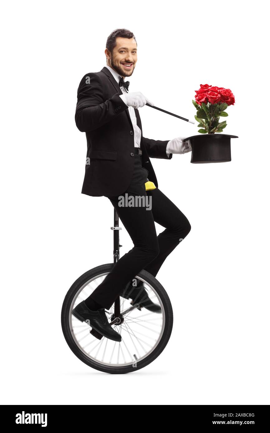 Magier, der mit Zauberstab, Hut und roten Rosen auf einem Einrad reitet und die auf weißem Hintergrund isolierte Kamera betrachtet Stockfoto