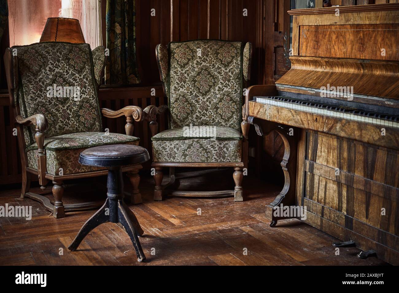 Vintage-Piano und Hocker auf rustikalem und Holzboden mit zwei alten Sesseln und einem schmutzigen Fenster dahinter Stockfoto