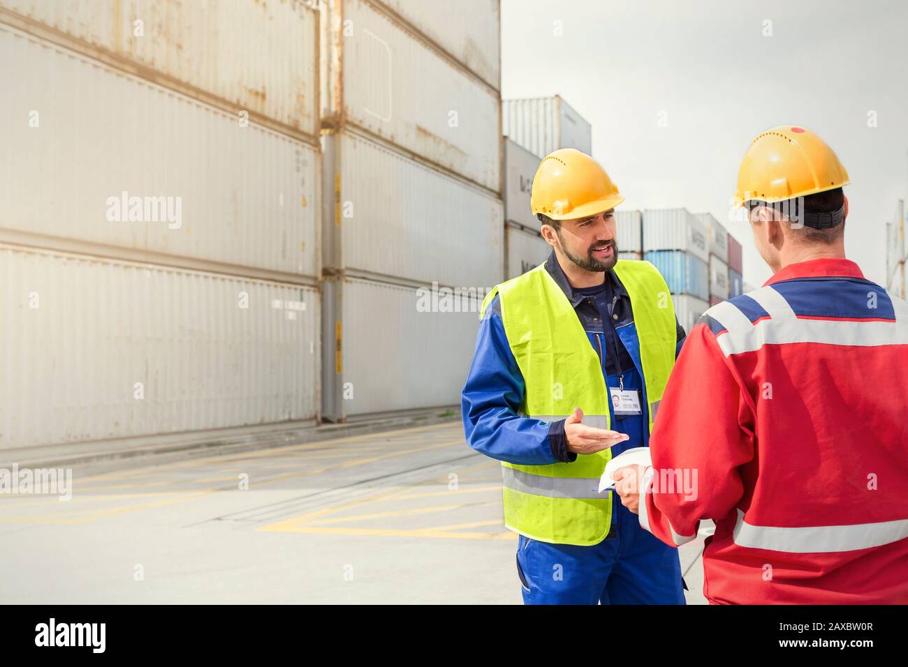 Hafenarbeiter sprechen in der Nähe von Frachtcontainern auf der sonnigen Werft Stockfoto