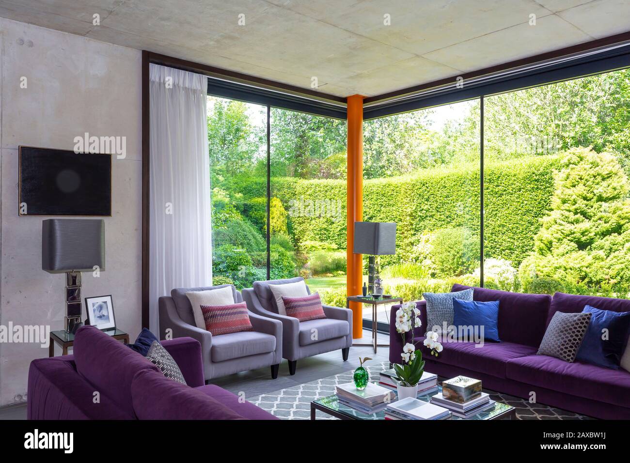 Modernes Wohnzimmer mit violetten Möbeln und Blick auf den sonnigen Garten Stockfoto