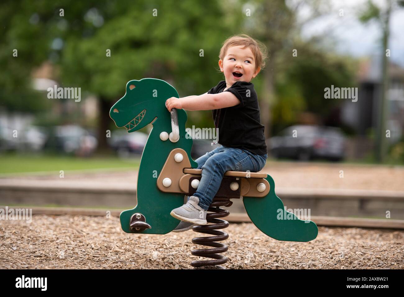 Unbeschwert süßes kleines Mädchen, das Dinosaurier-Spielzeug auf dem Spielplatz reitet Stockfoto