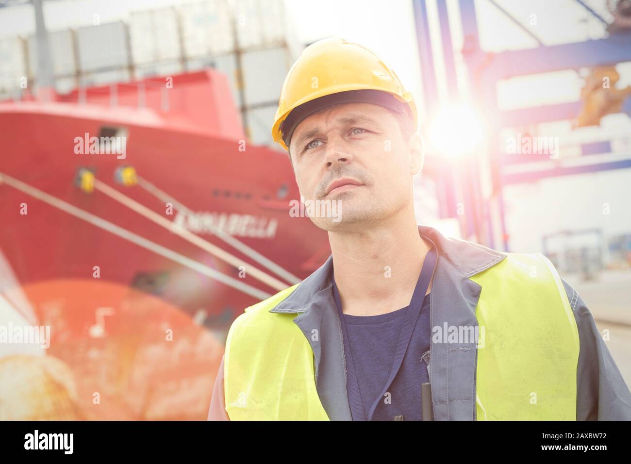 Ernsthafter Hafenarbeiter unter dem Containerschiff am Handelsdock Stockfoto
