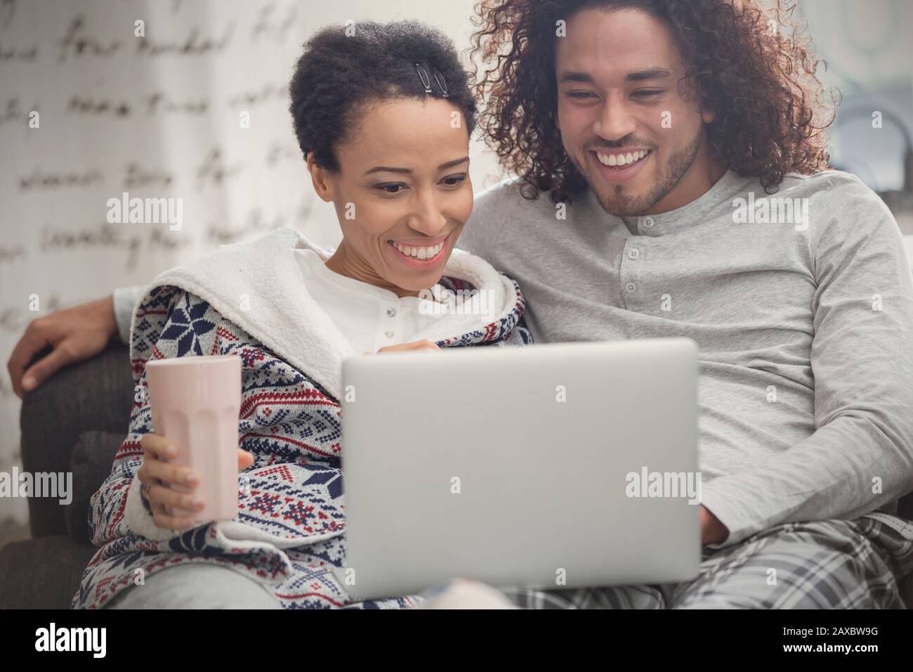 Glückliches Paar in Schlafanzug entspannend, mit Laptop auf Sofa Stockfoto