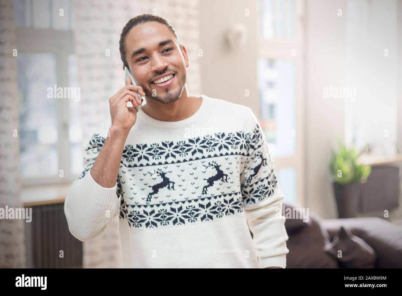 Lächelnder junger Mann im Weihnachts-Pullover telefoniert Stockfoto