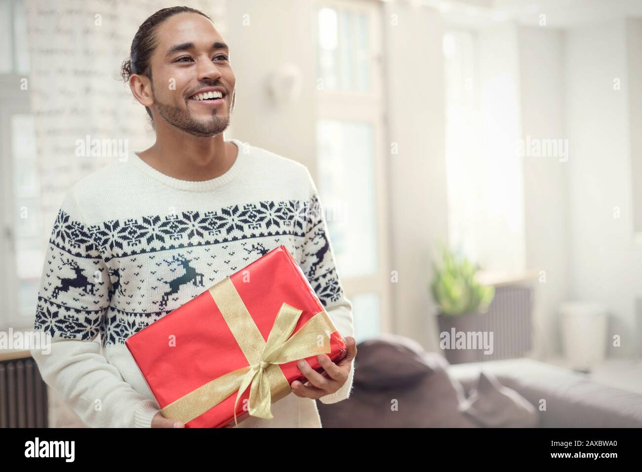 Junger Mann im Weihnachts-Pullover mit Geschenk Stockfoto