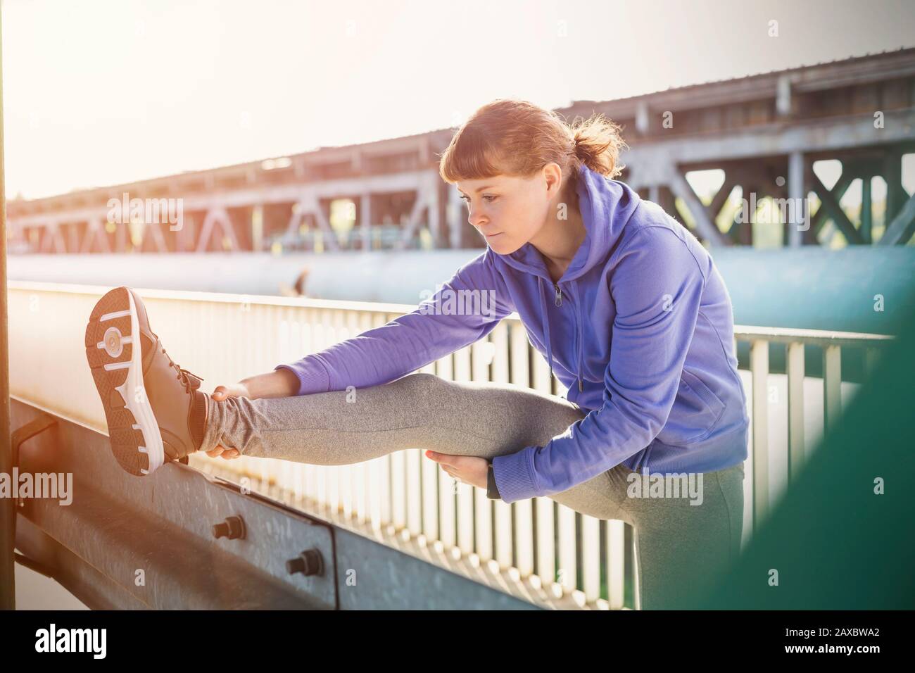 Junge weibliche Läuferin streckt sich das Bein auf dem städtischen Geländer Stockfoto