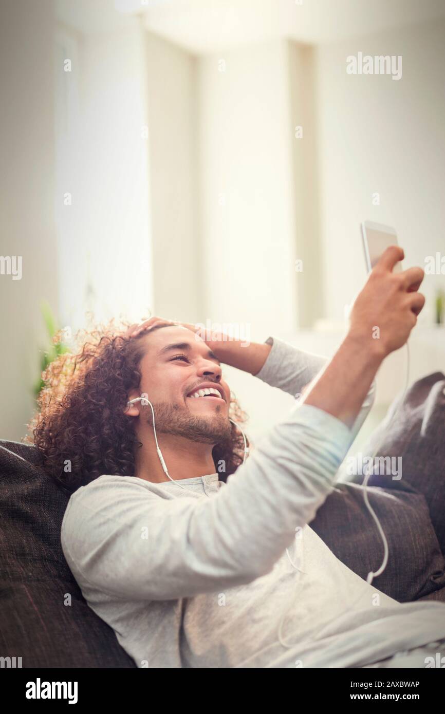 Fröhlicher junger Mann, der Musik mit Kopfhörern und MP3-Player auf dem Sofa hört Stockfoto