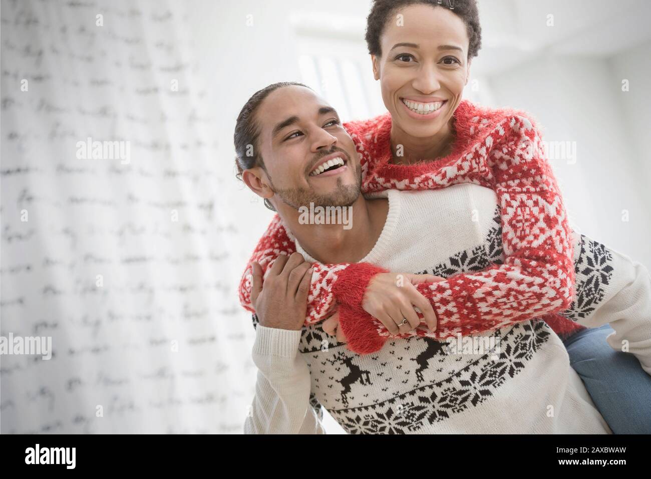 Portrait fröhliches, verspieltes Paar in Weihnachts-Pullovern mit Huckepack Stockfoto