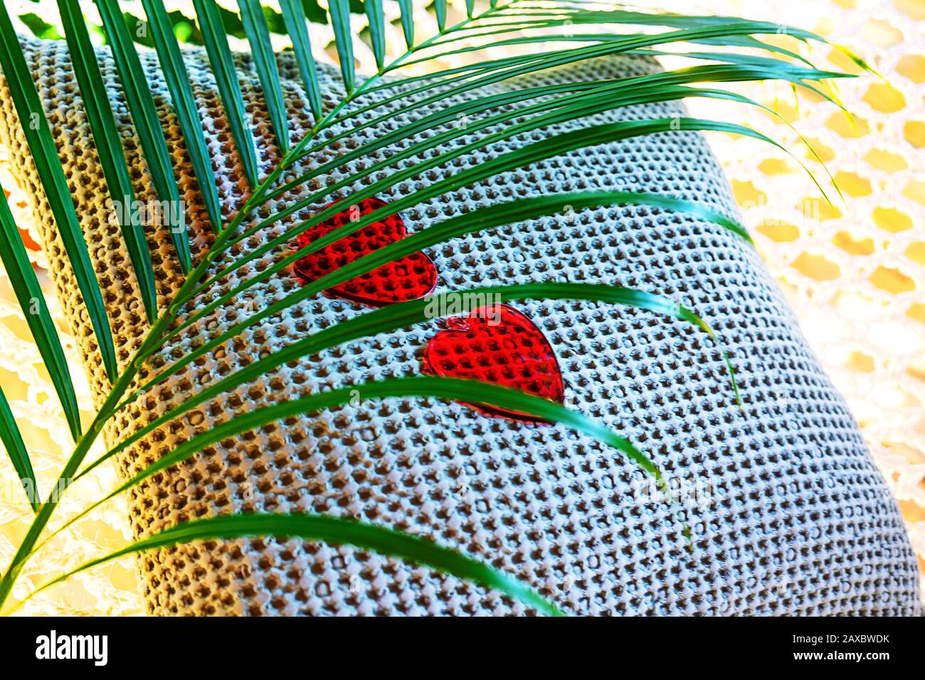 Zwei rote Herzen und Palmblätter auf dekorativem Kissen und Hängematte. Valentinskarte mit tropischem Naturhintergrund. Flaches Layout, Draufsicht, Kopierbereich. Stockfoto