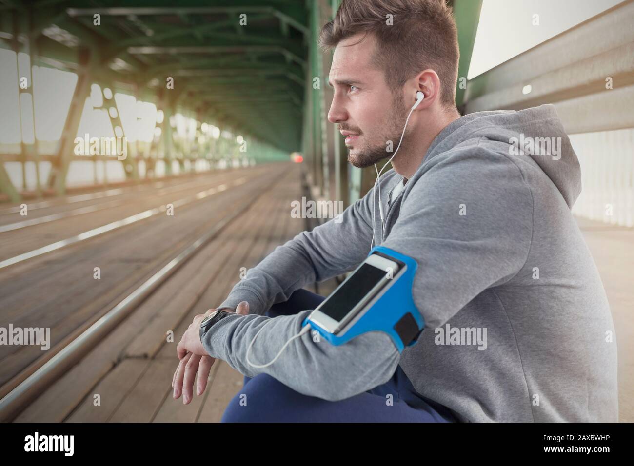 Junger männlicher Läufer ruht und hört Musik mit Kopfhörern und MP3-Player auf dem Bahnsteig Stockfoto