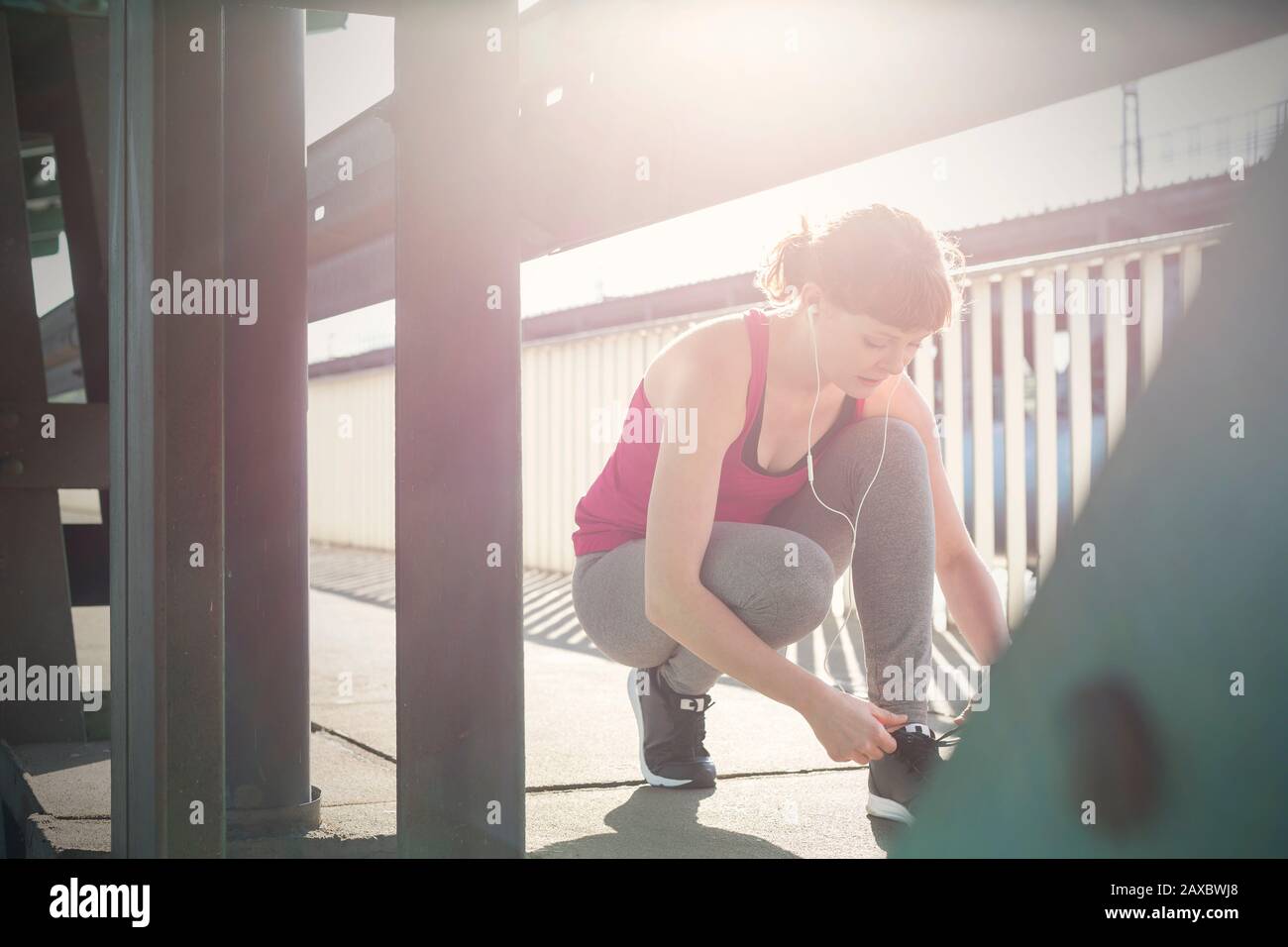 Junge Läuferin, die Schuhe auf dem sonnigen städtischen Bürgersteig bindet Stockfoto