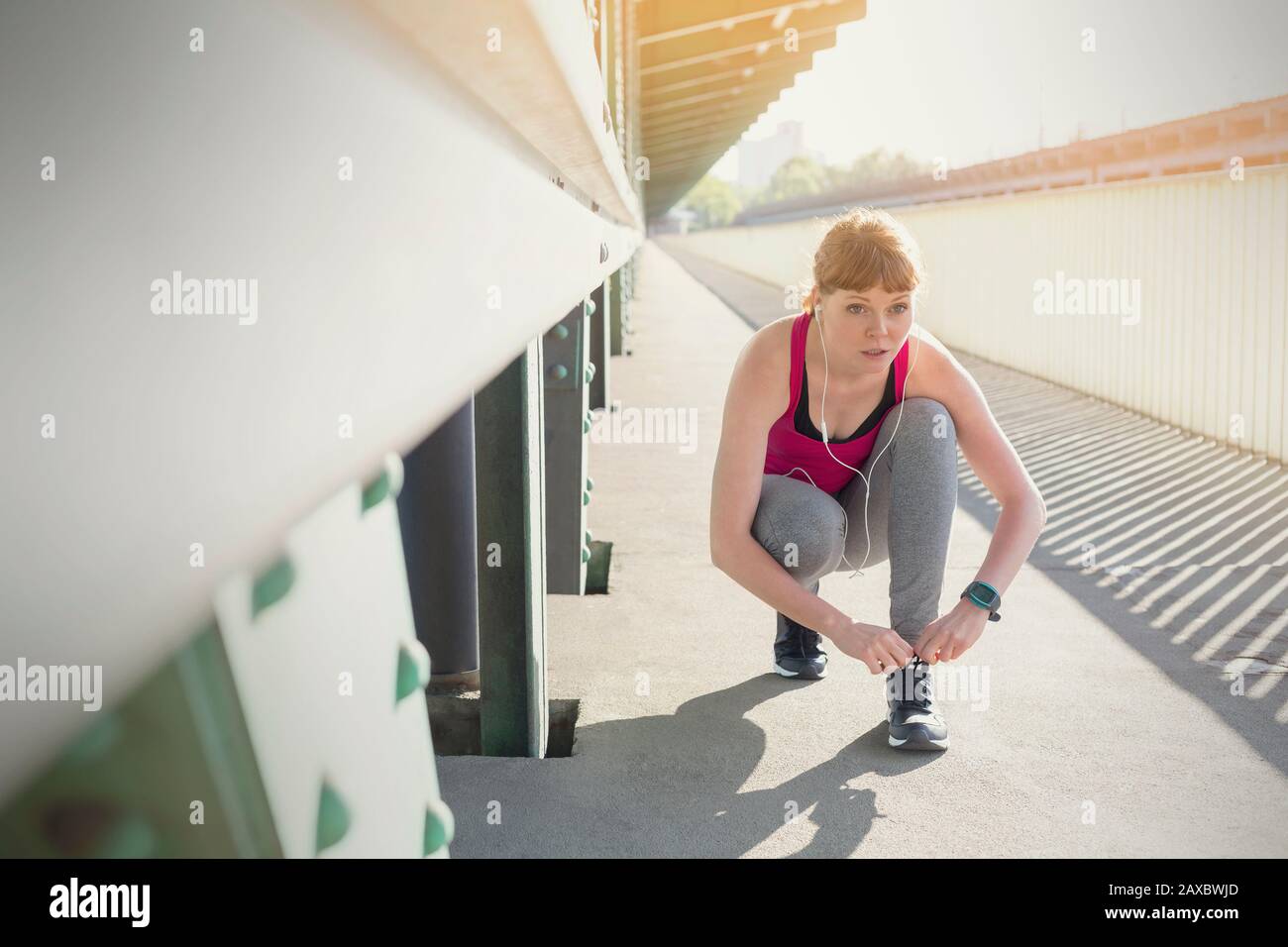 Gebundener junger Läufer, der den Schuh auf dem sonnigen Bahnsteig bindet Stockfoto