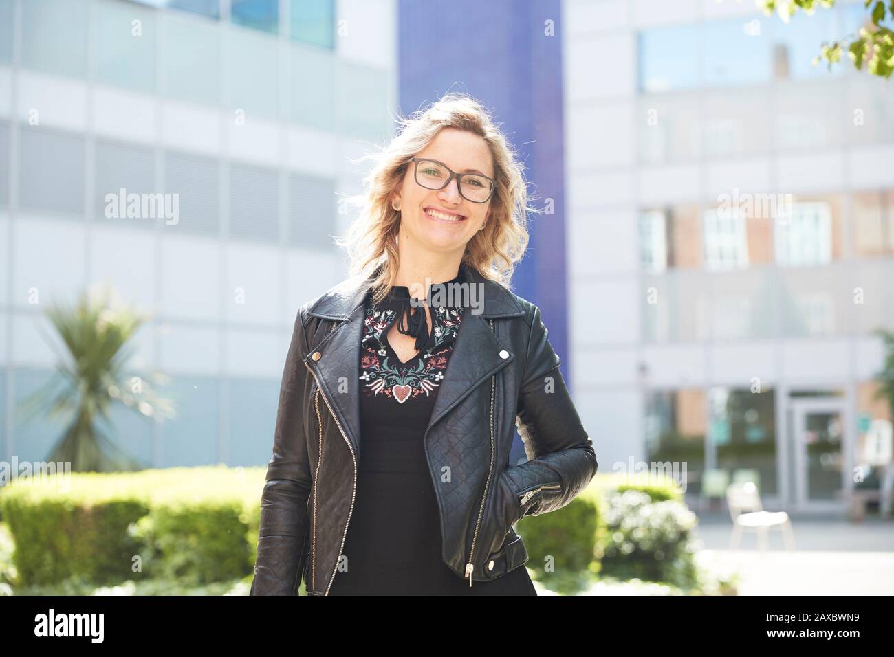 Portrait selbstbewusste Frau in Lederjacke außerhalb des sonnigen Gebäudes Stockfoto