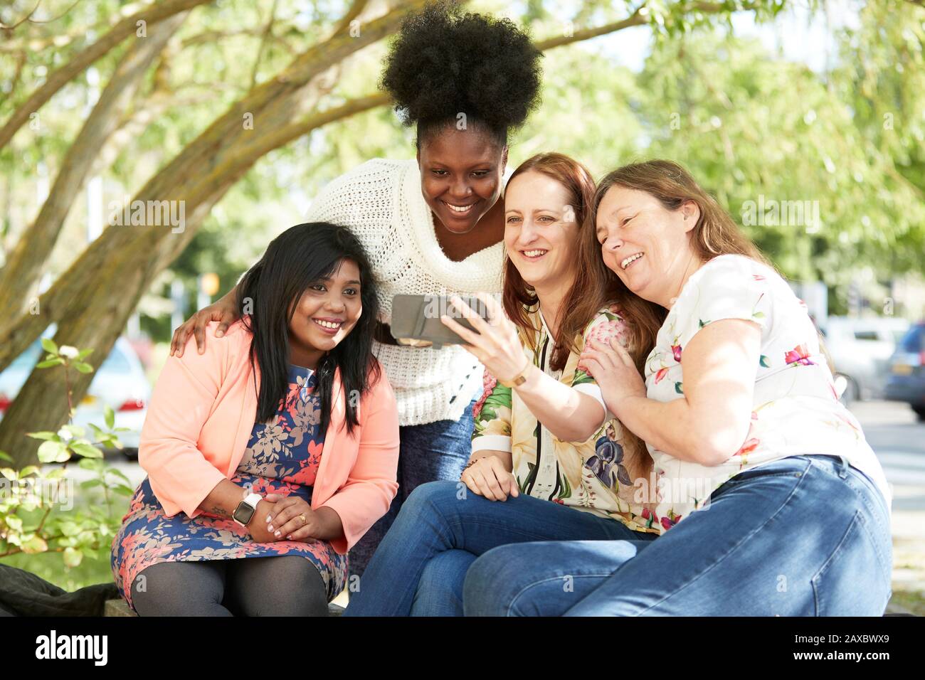 Glückliche weibliche Freunde, die im Park ein Smartphone benutzen Stockfoto