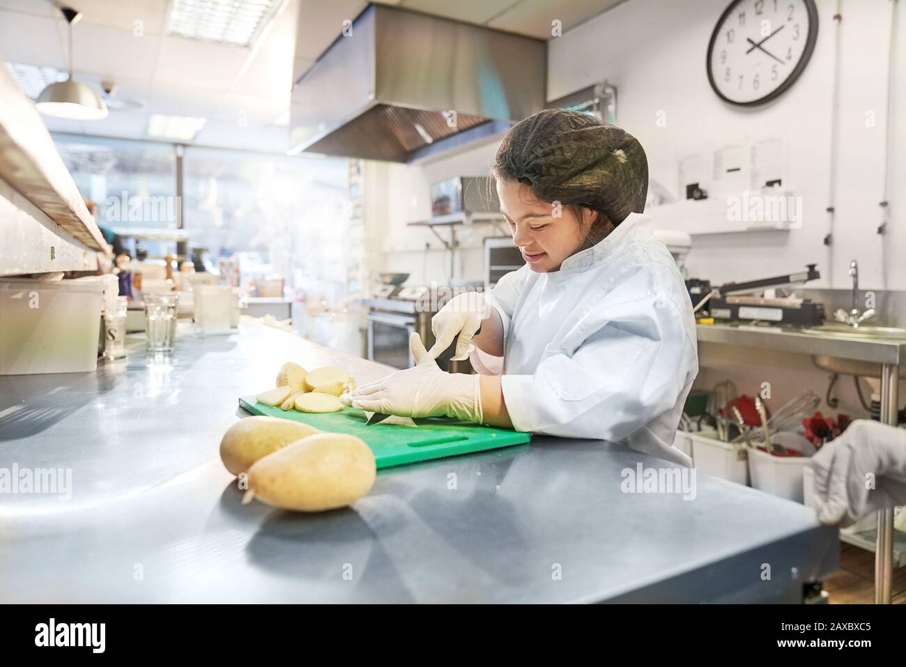 Junge Frau mit Down-Syndrom, die Kartoffeln in der Café-Küche schneidet Stockfoto