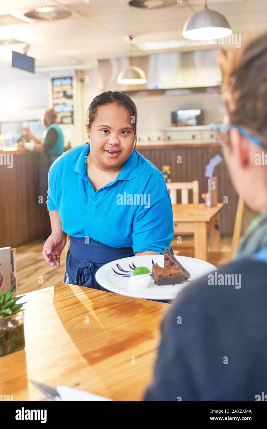 Junger weiblicher Server mit Down-Syndrom, der Dessert im Café serviert Stockfoto