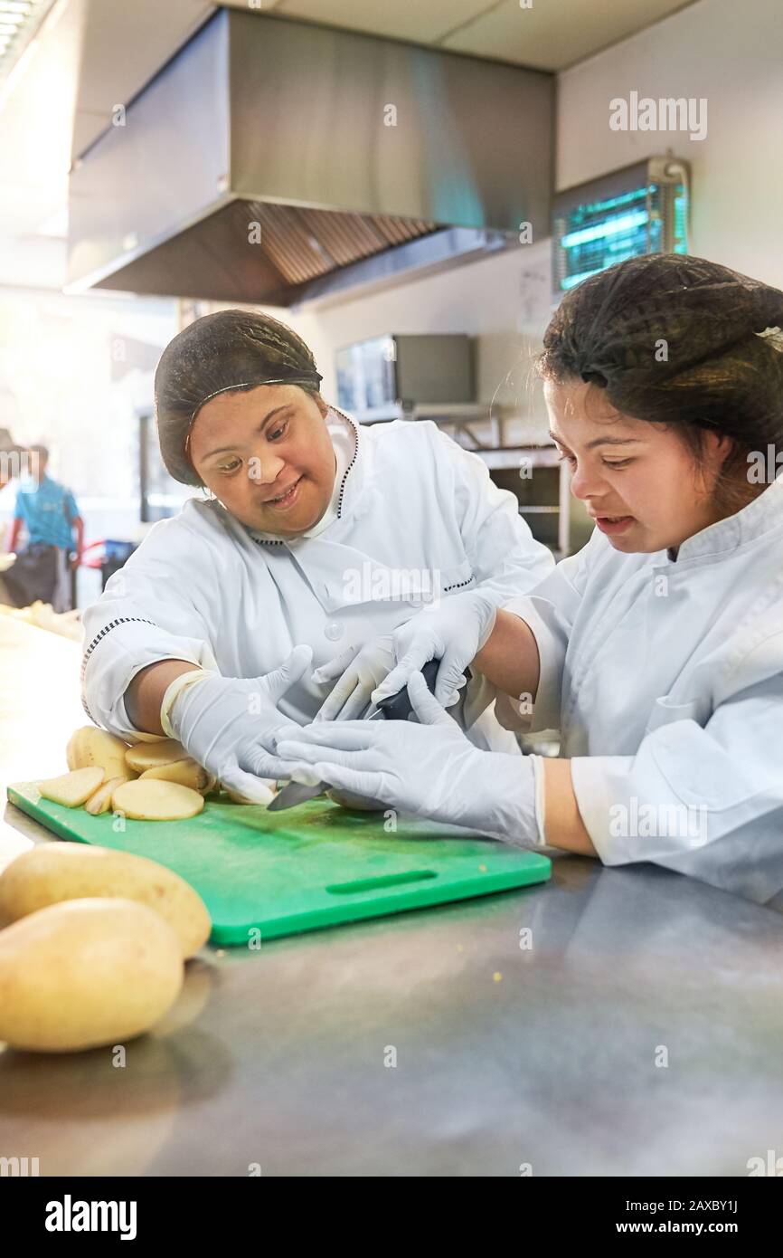 Junge Frauen mit Down-Syndrom, die Kartoffeln in der Café-Küche schneiden Stockfoto