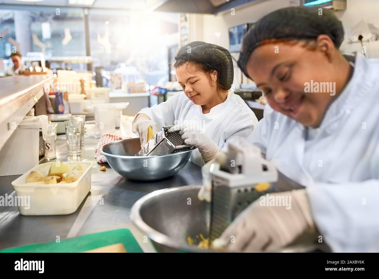 Lächelnde junge Frauen mit Daunen-Syndrom, die Käse in der Café-Küche reiben Stockfoto