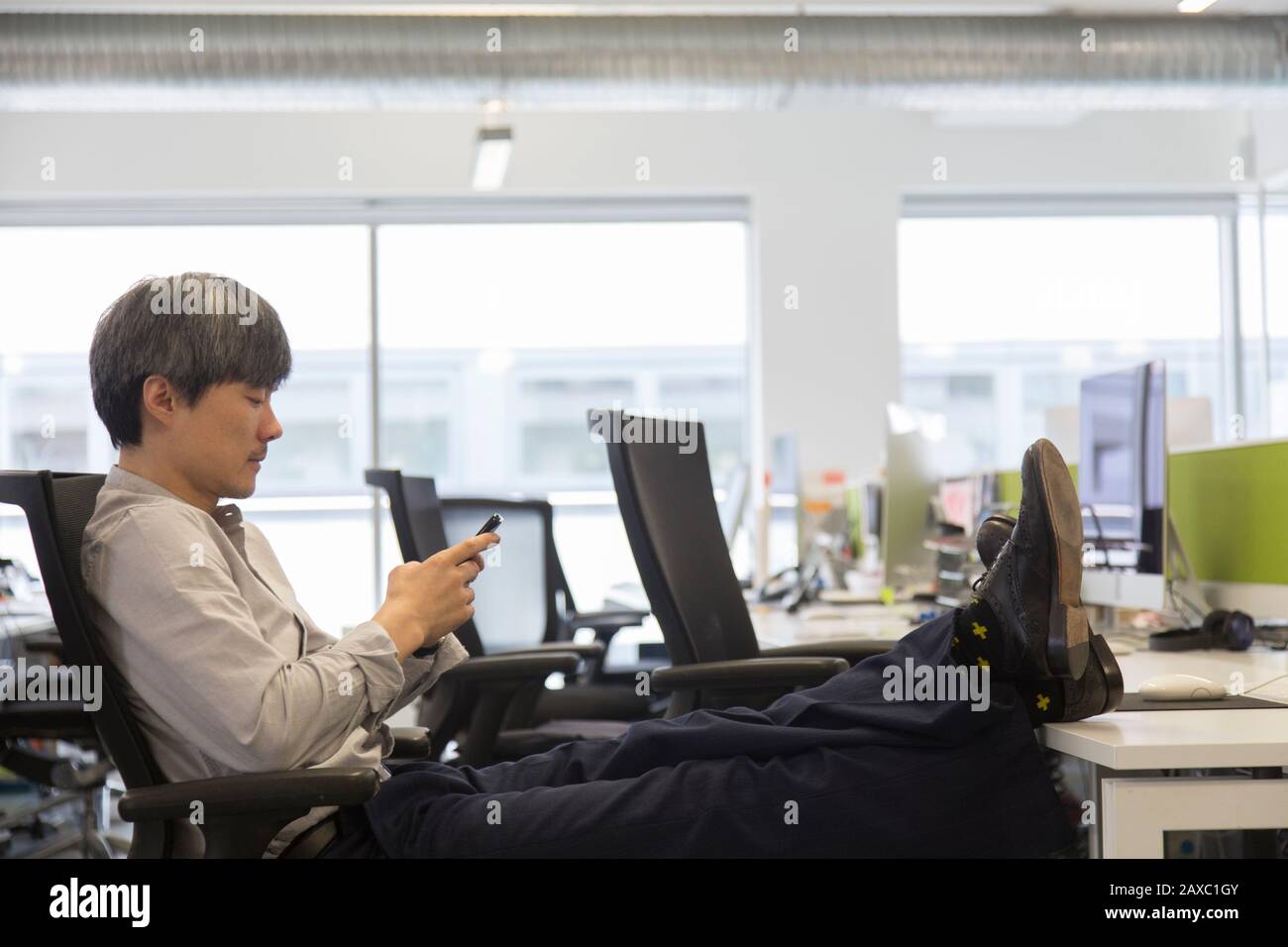 Geschäftsleute, die ein Smartphone verwenden, mit Füßen nach oben auf dem Schreibtisch Stockfoto