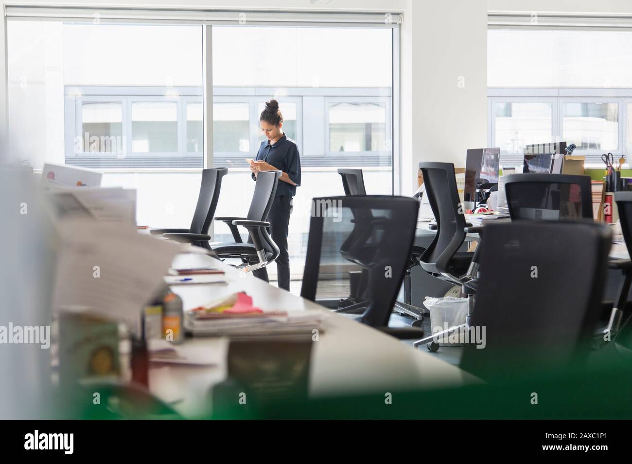 Geschäftsfrau mit Smartphone im sonnigen Bürofenster Stockfoto