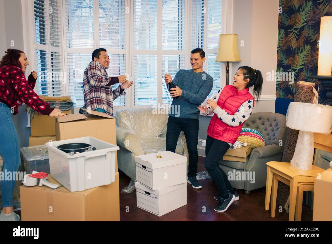 Fröhliche Freunde, die ihr Haus umziehen und mit Champagner feiern Stockfoto